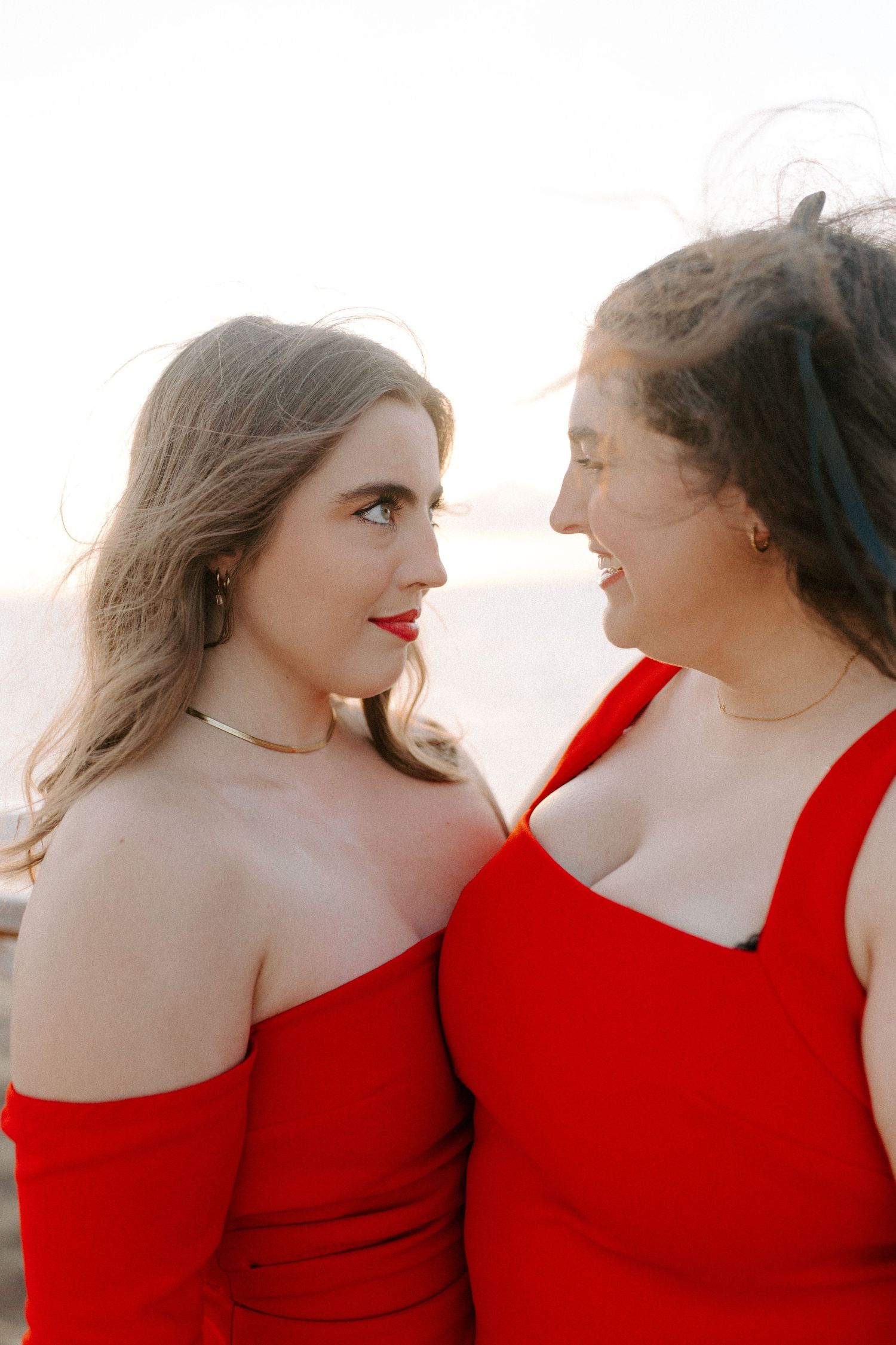 Close-up portrait of two people wearing red dresses gazing at each other with affection.