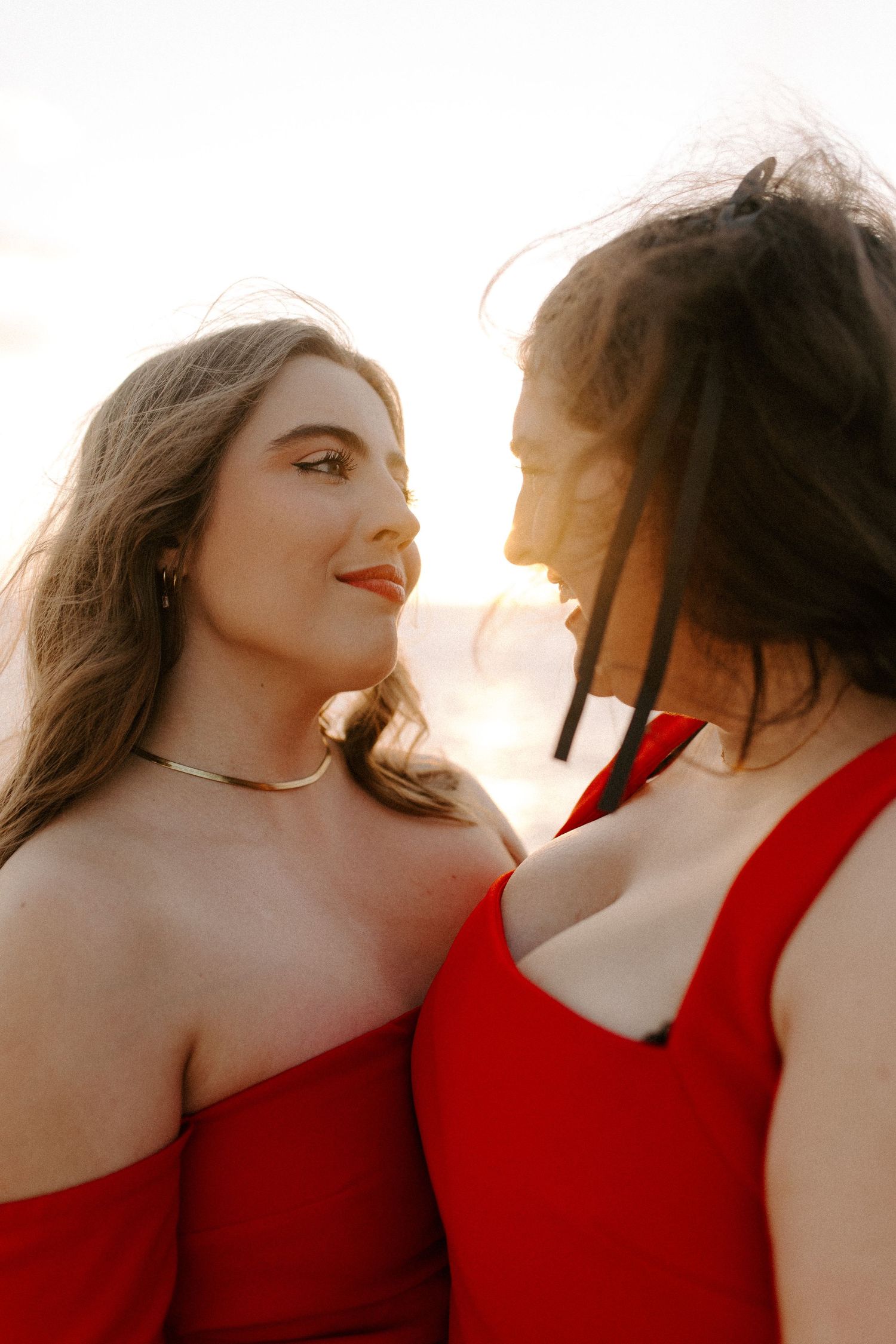 Romantic sunset portrait of two people in red dresses smiling at each other.