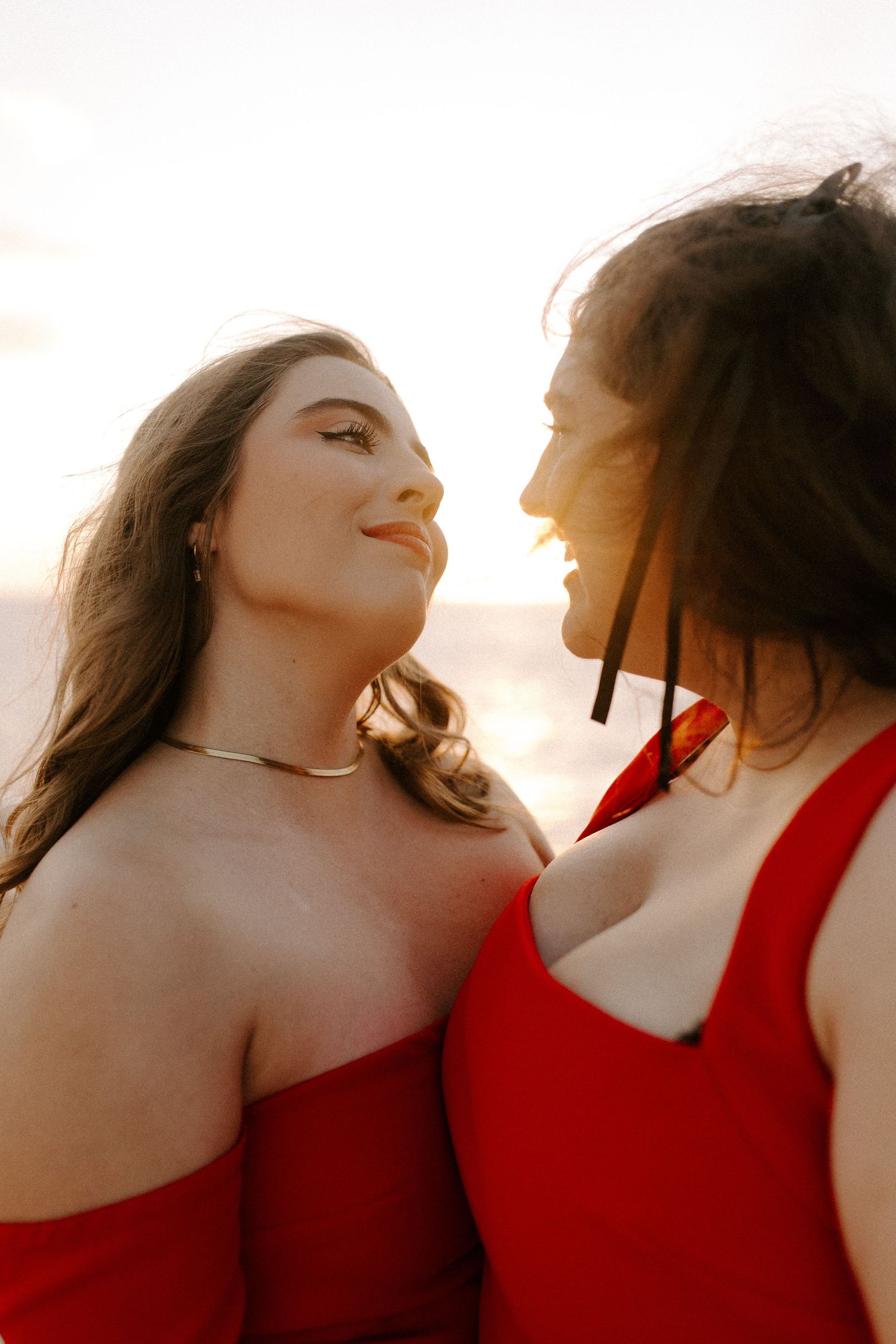 Close-up shot of two people in red formal wear sharing a tender moment at sunset.