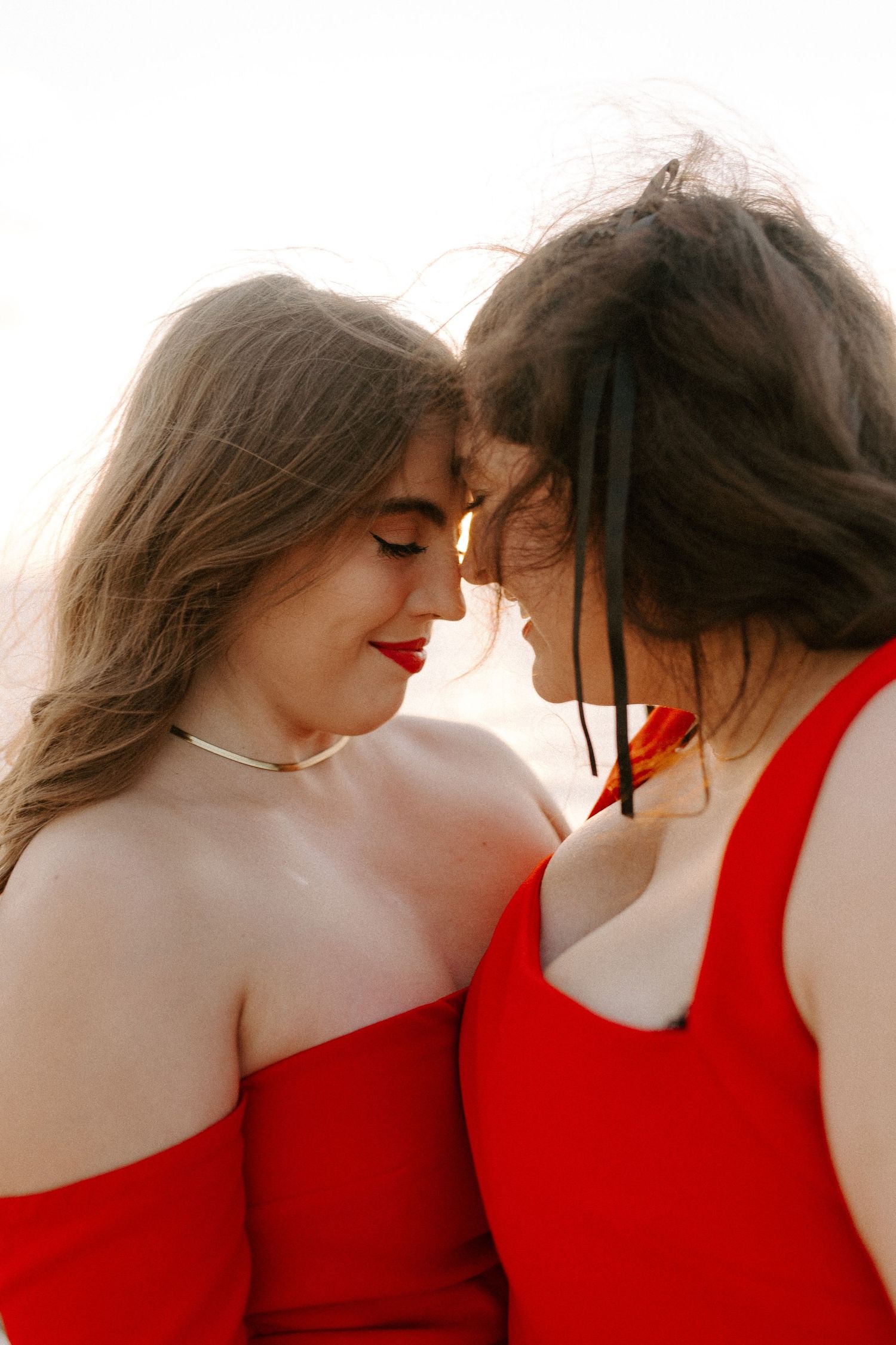 Intimate moment between two people in red dresses with foreheads touching.