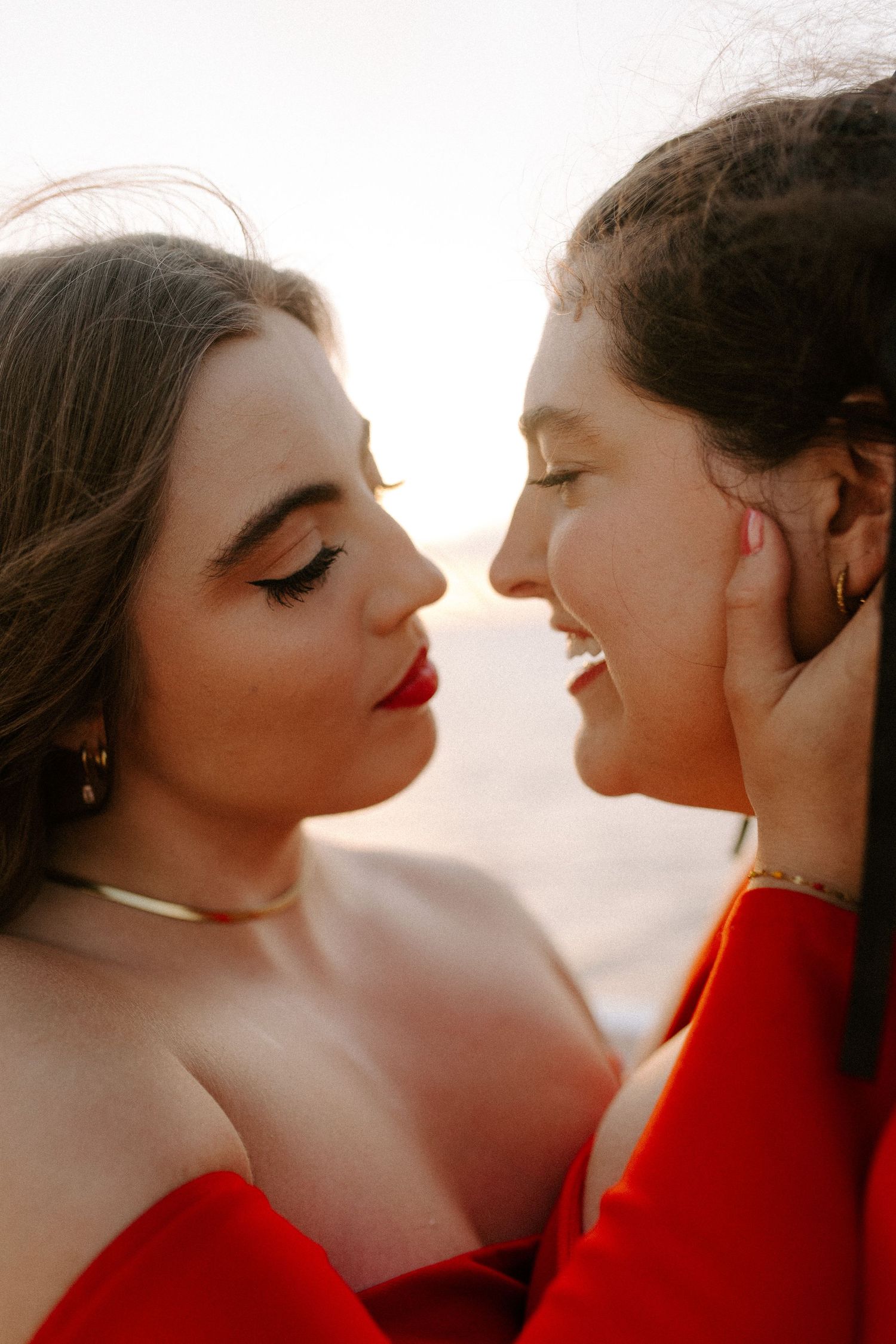 An intimate portrait of a couple in coordinated red outfits sharing a tender moment at sunset.