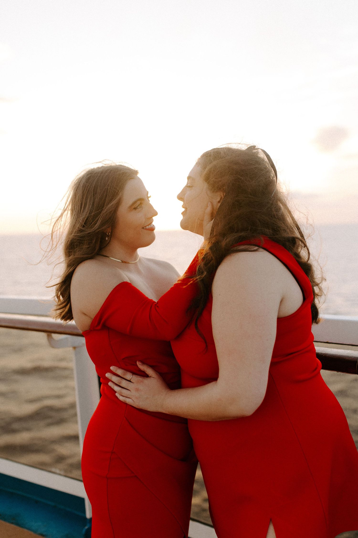 Two people in matching red outfits share a romantic moment on a boat deck with ocean views.