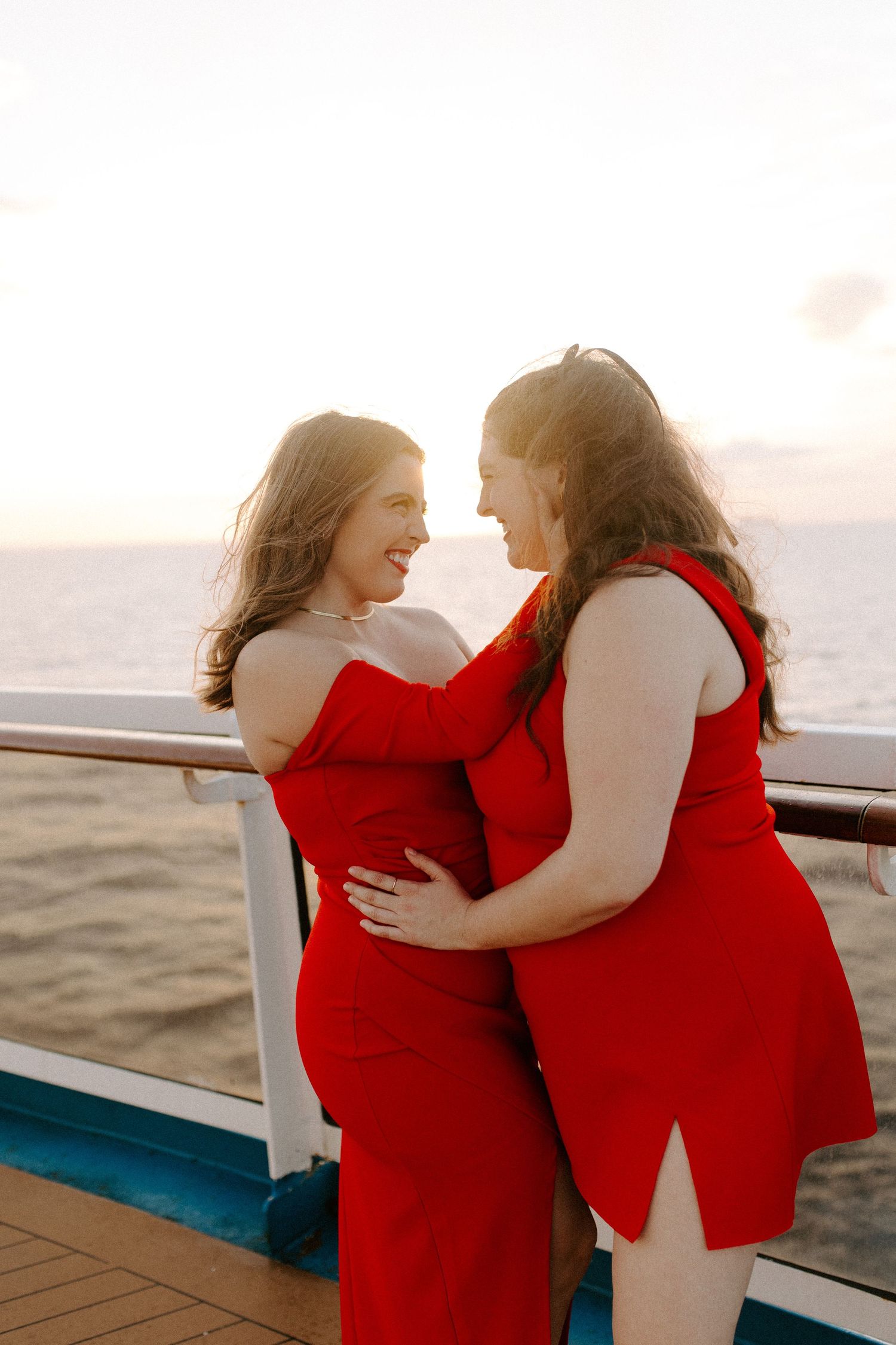 A happy couple in red outfits laughing and embracing on a cruise ship deck.