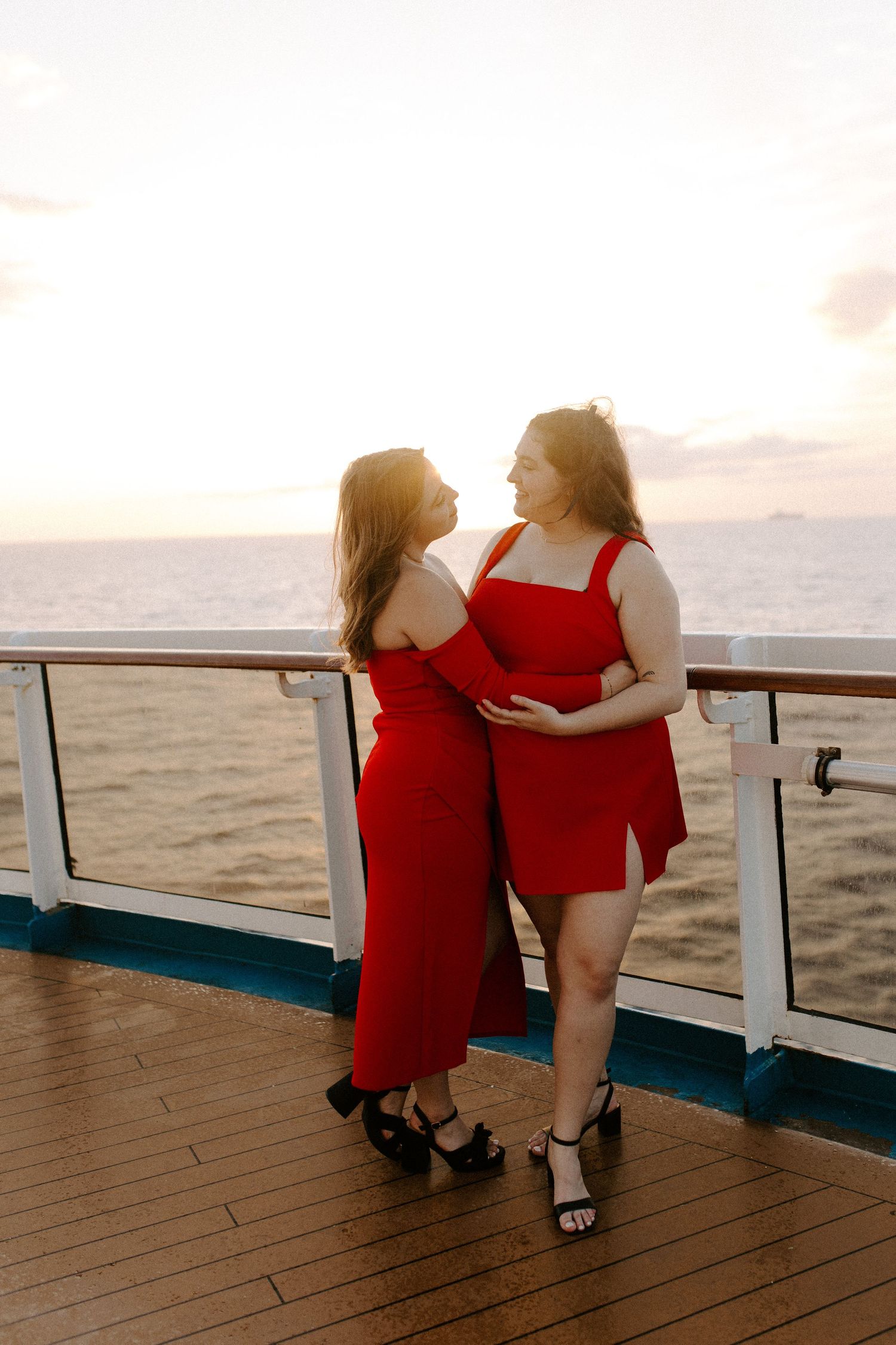 A couple in elegant red outfits sharing an intimate dance on a cruise ship deck at sunset.