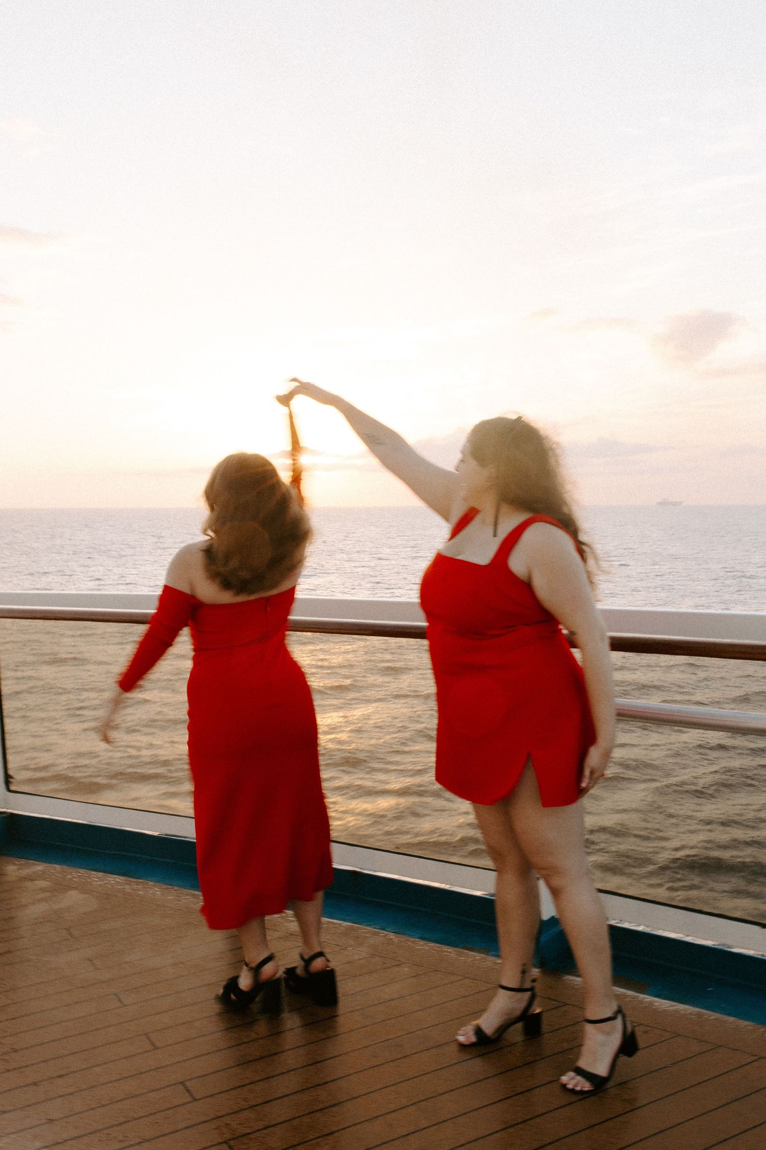 Two people in matching red outfits dancing with raised arms on a cruise ship deck.