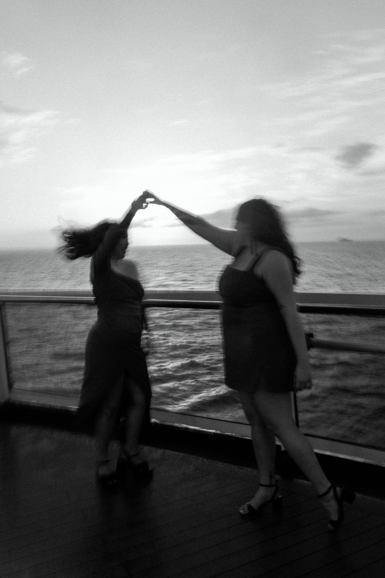 Black and white photo of playful dancing figures on a ship deck against an ocean backdrop.