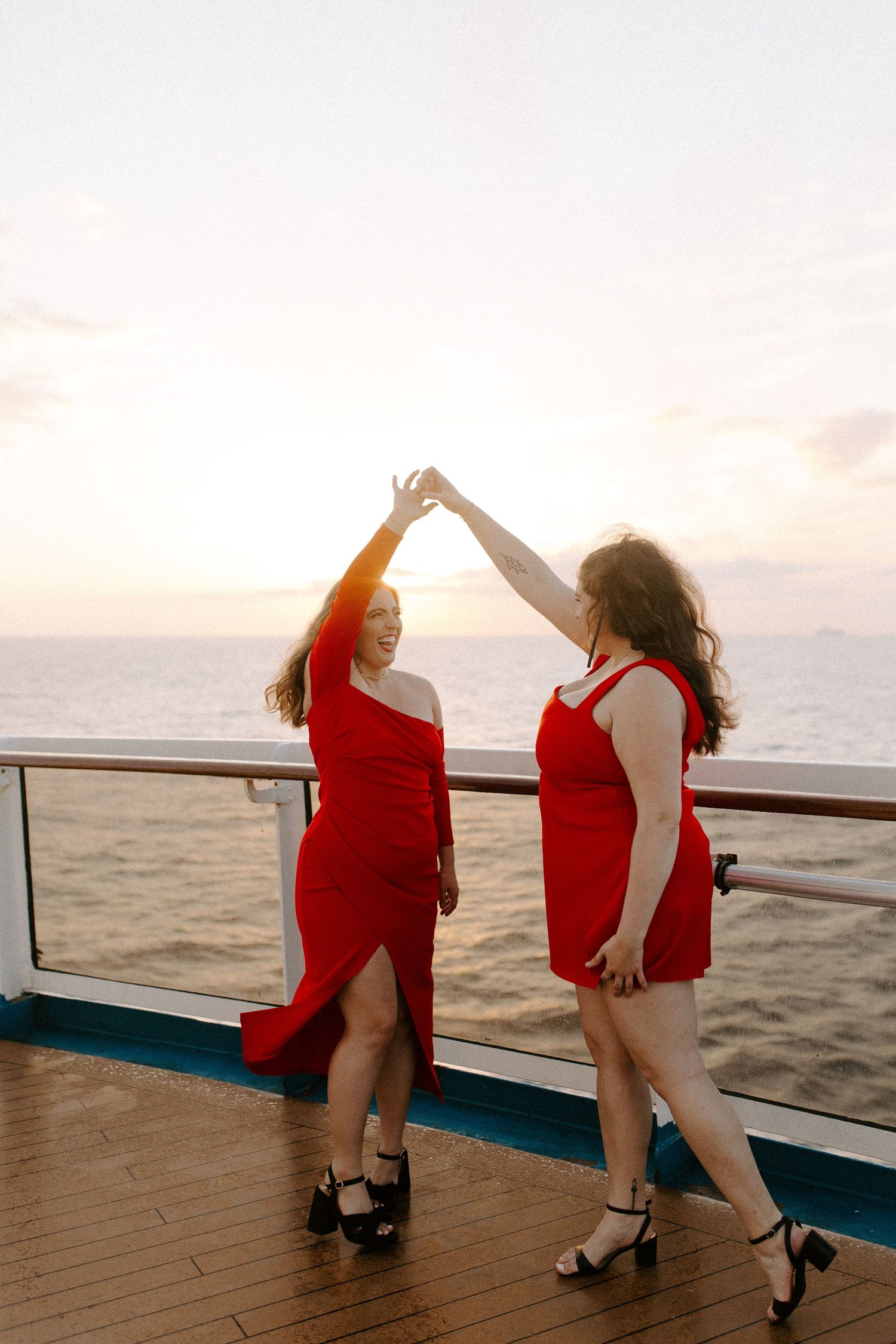 Two people in red dresses dancing together on a cruise ship deck at sunset.