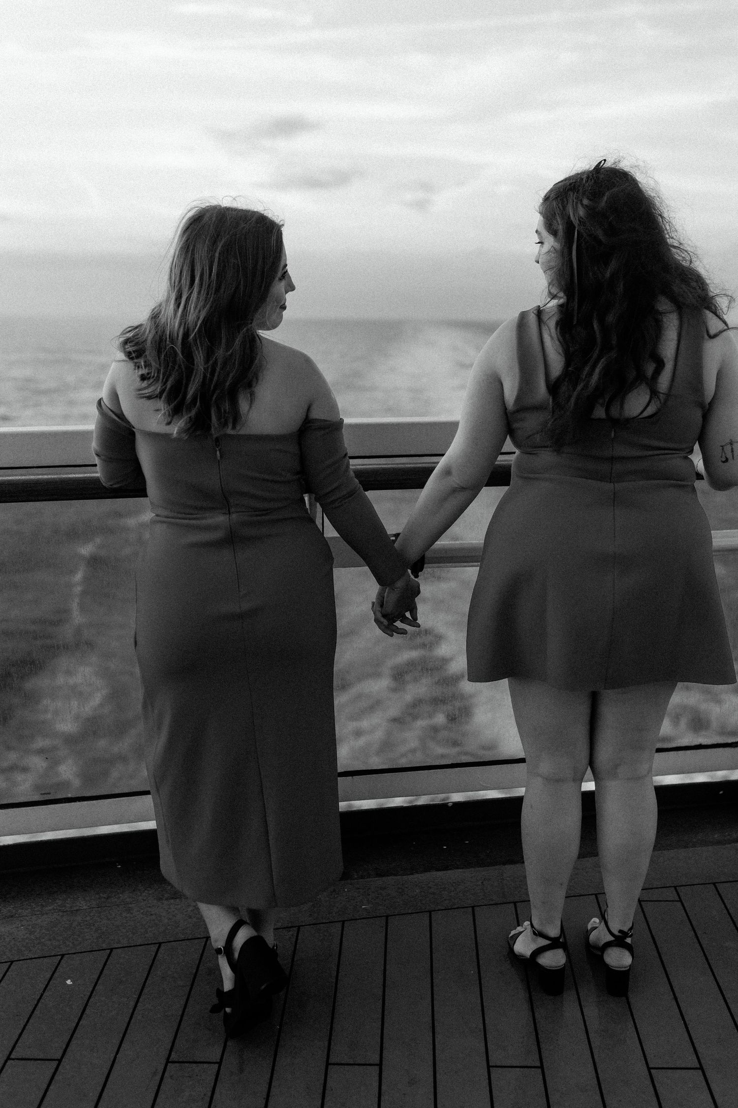 A black and white photo of two people holding hands while viewing the ocean from a ship's deck.