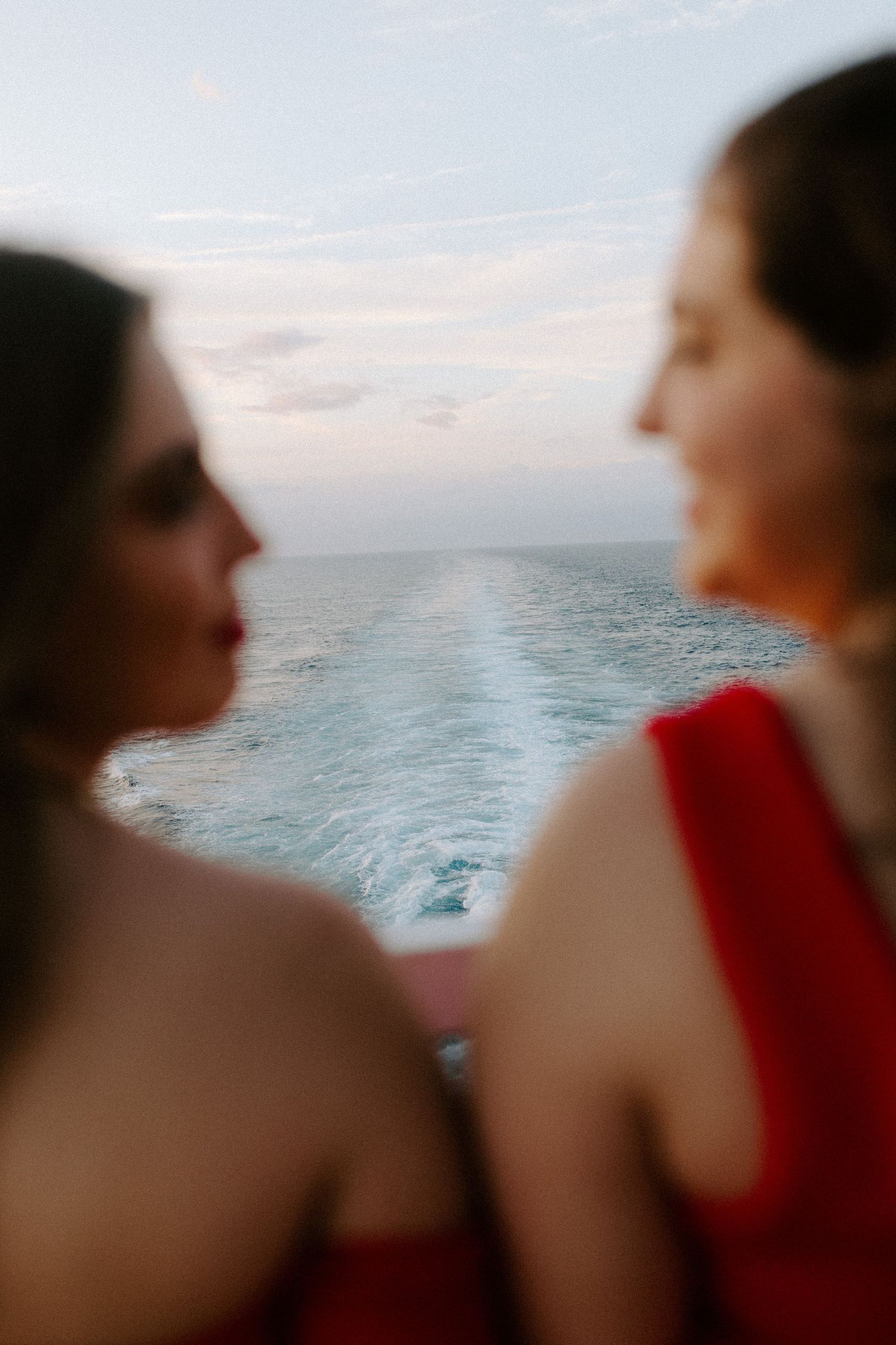 Close-up profile view of two people in red attire watching the ocean wake from a ship's deck.