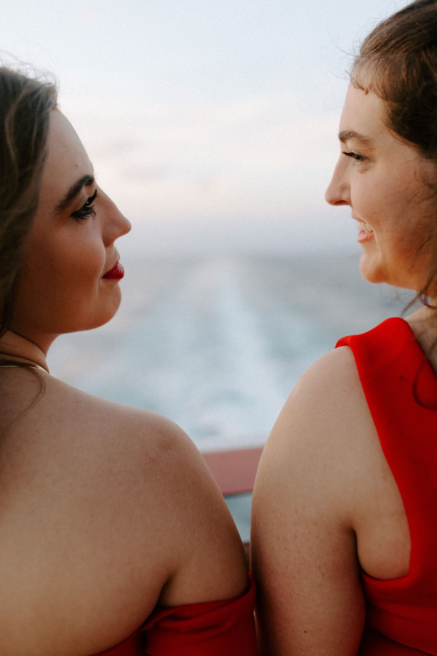 Close-up side view of two people in red dresses sharing a moment on a cruise ship deck.