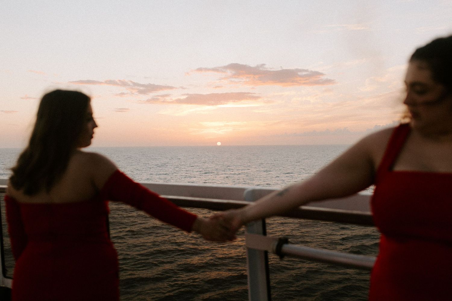 Two friends in matching red dresses share moment during sunset cruise.