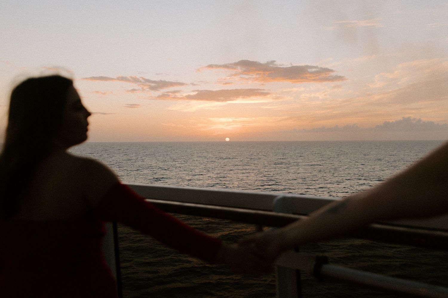 Two silhouettes holding hands while watching a romantic ocean sunset from a balcony or deck.