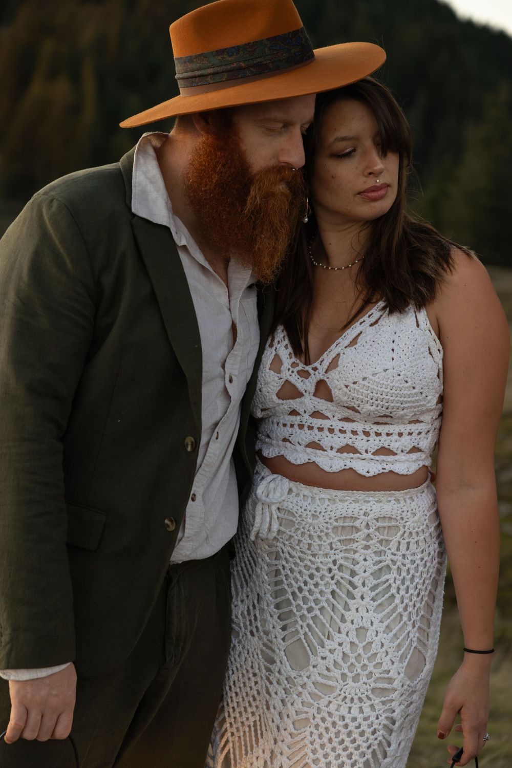 Intimate moment captured between couple in bohemian wedding attire on mountain at sunset.