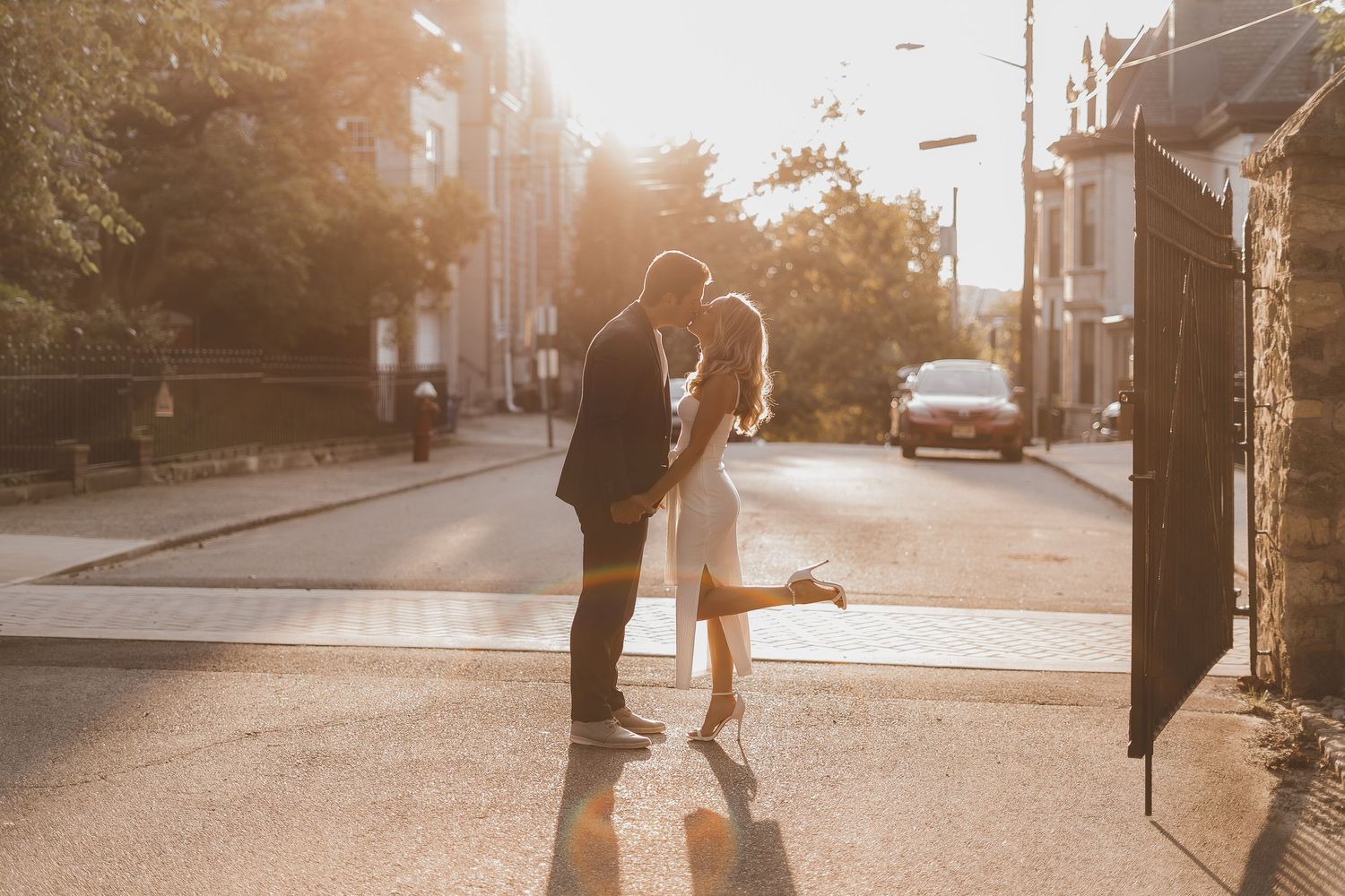 A romantic urban scene during golden hour with silhouetted couple embracing on a sunlit street corner.