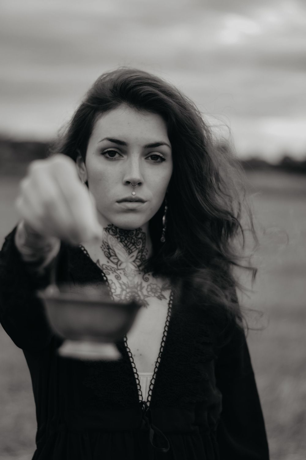 Moody black and white portrait of a woman in dark clothing with dramatic lighting and windswept hair.