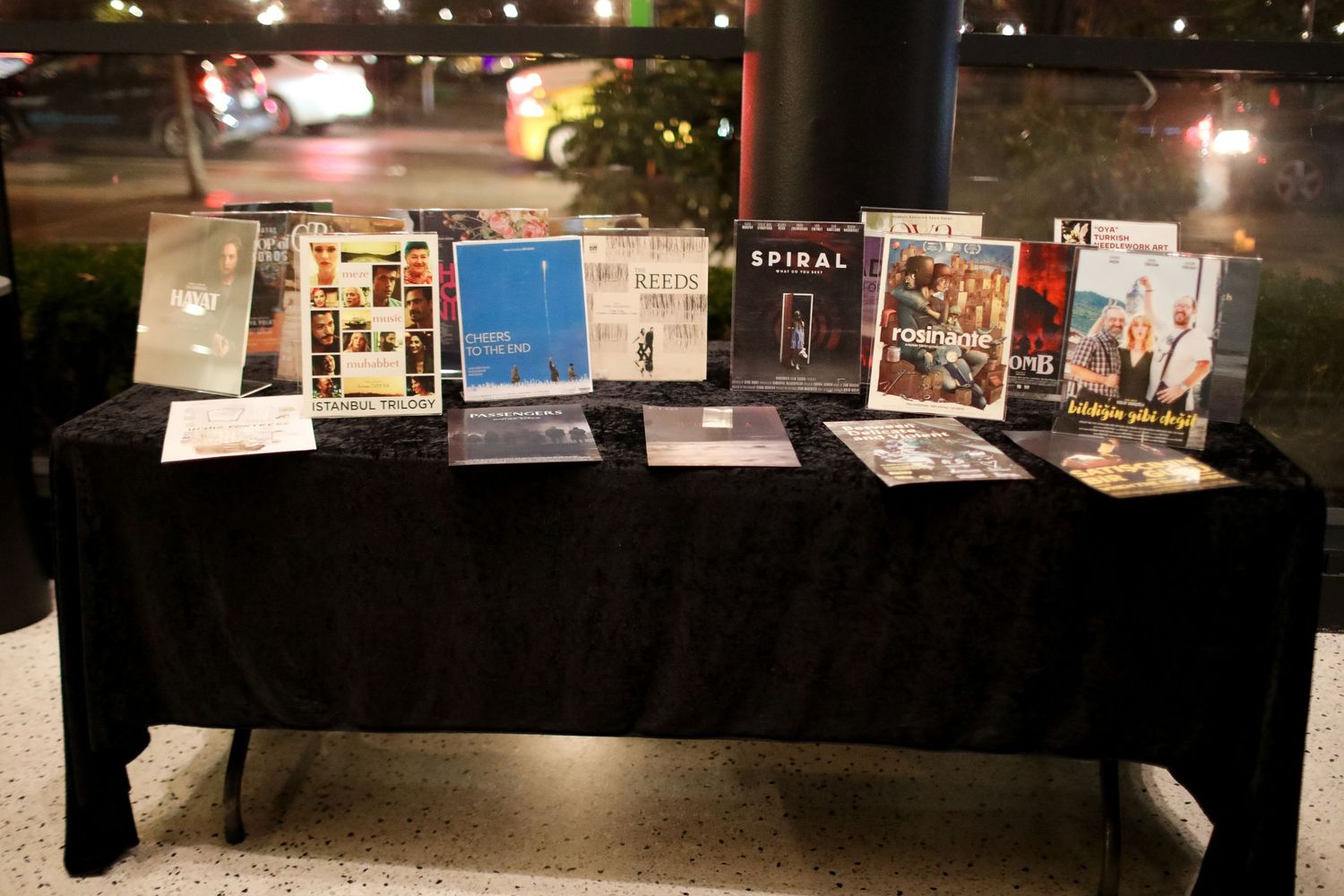Several books on display arranged on a black cloth-covered table at night, illuminated in a dimly lit space.