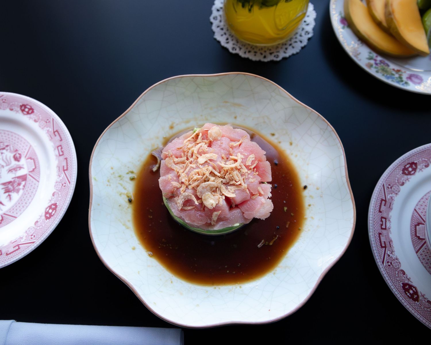 Pink garnished sushi roll served on a white plate with dark soy sauce.