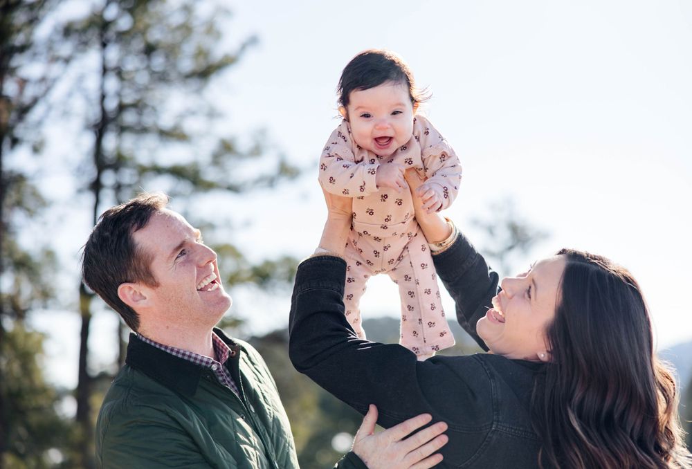 Candid moment of parents playfully lifting their baby during a mountain photoshoot.