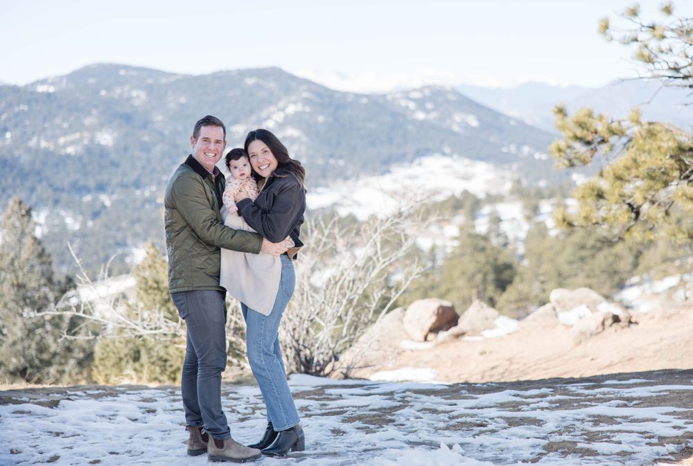 Couple embracing on rocky overlook with mountain vista behind them.