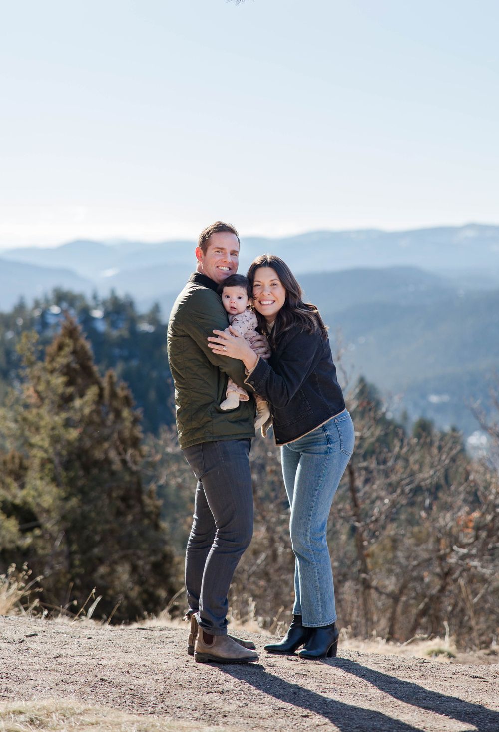 Family portrait in the mountains with snow-capped peaks and evergreen trees in the background.