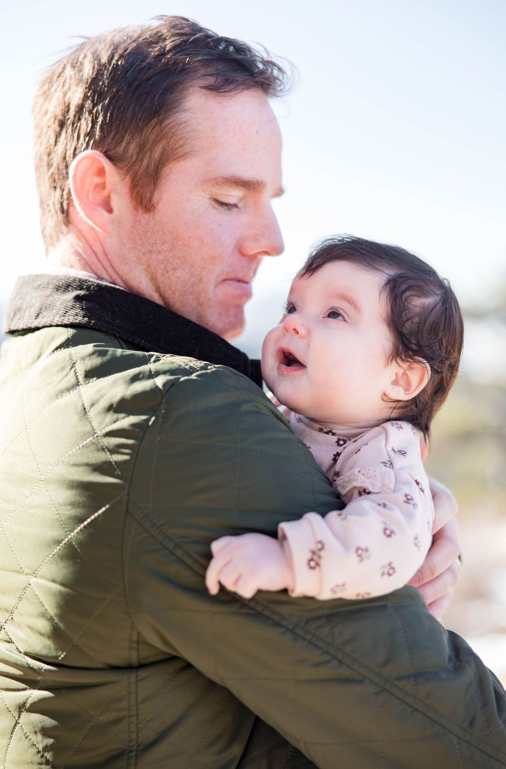 Sweet moment between parent and baby wearing floral onesie against mountain backdrop.