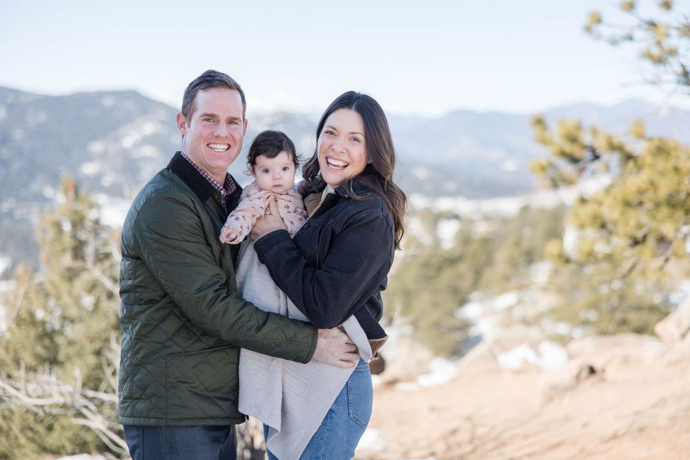 Family of three posing together on mountain overlook in winter.