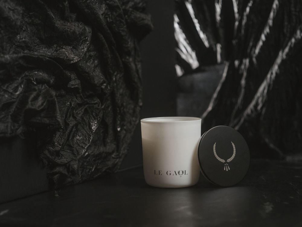 A minimalist white ceramic candle holder and black stone sit against a dark moody background with plant shadows.