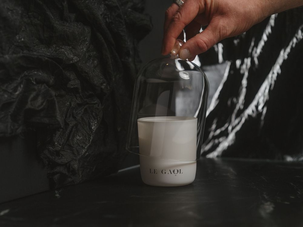 Hand pouring cream from a small metal pitcher into a white ceramic coffee cup against a dark background.