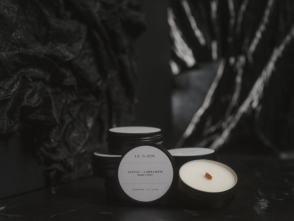 Three white minimalist candles in dark matte containers arranged on a black surface with moody lighting and shadows.