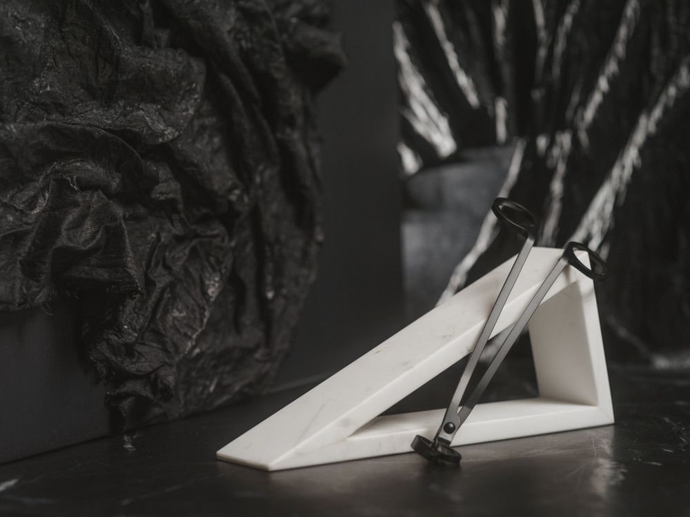 A white paper airplane rests on a dark surface with dramatic lighting and shadows in black and white photography.
