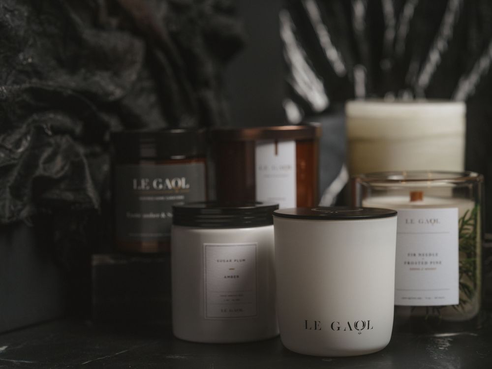 Luxury scented candles in white and brown containers arranged against a dark moody background with botanical shadows.