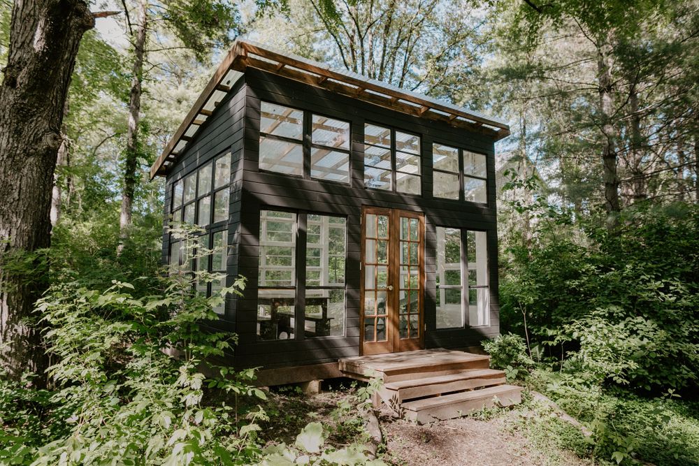 Modern glass greenhouse cabin nestled in lush forest setting.