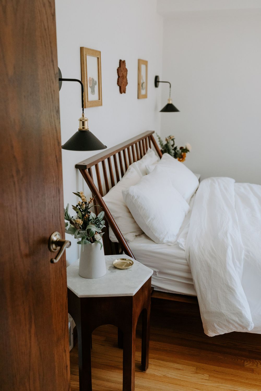 Cozy bedroom corner with wooden headboard, white bedding, and wall sconces.