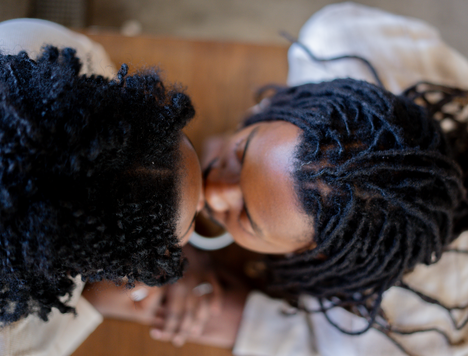 Overhead view of two Black women with natural and braided hair touching foreheads in an intimate moment.
