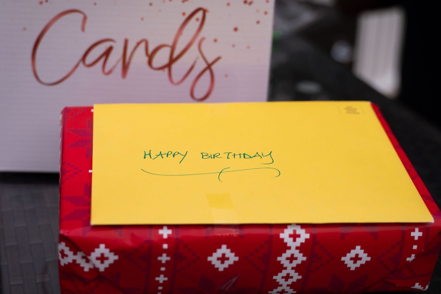 A yellow birthday card sits atop a red box decorated with diamond patterns.