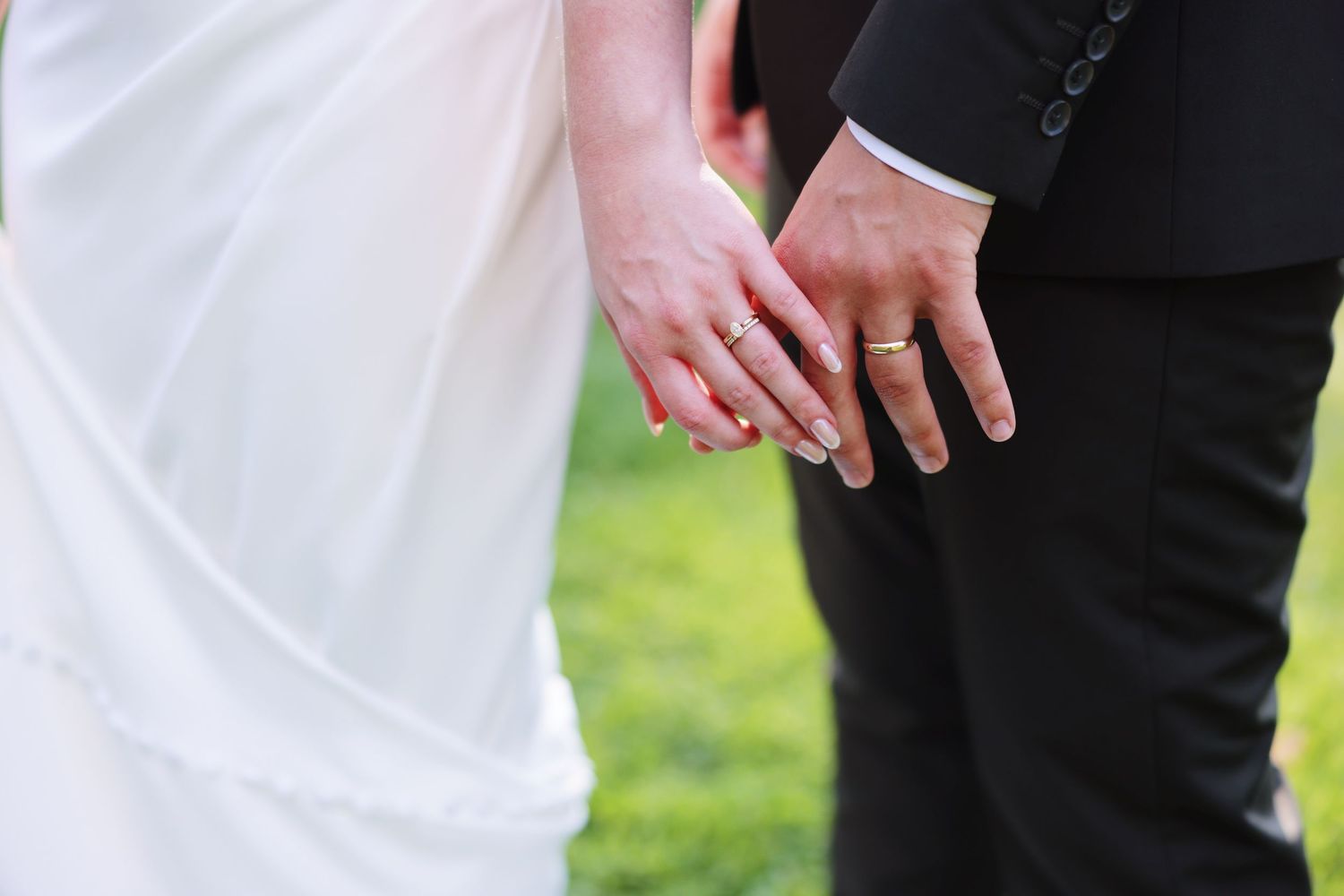 A couple in formal wedding attire holds hands while walking together in a garden setting.