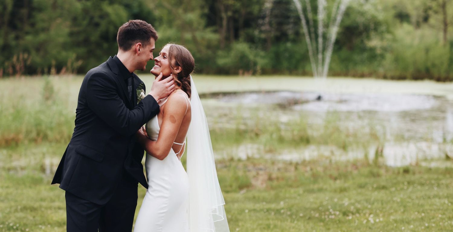 Newlyweds share intimate moment near fountain during outdoor wedding.