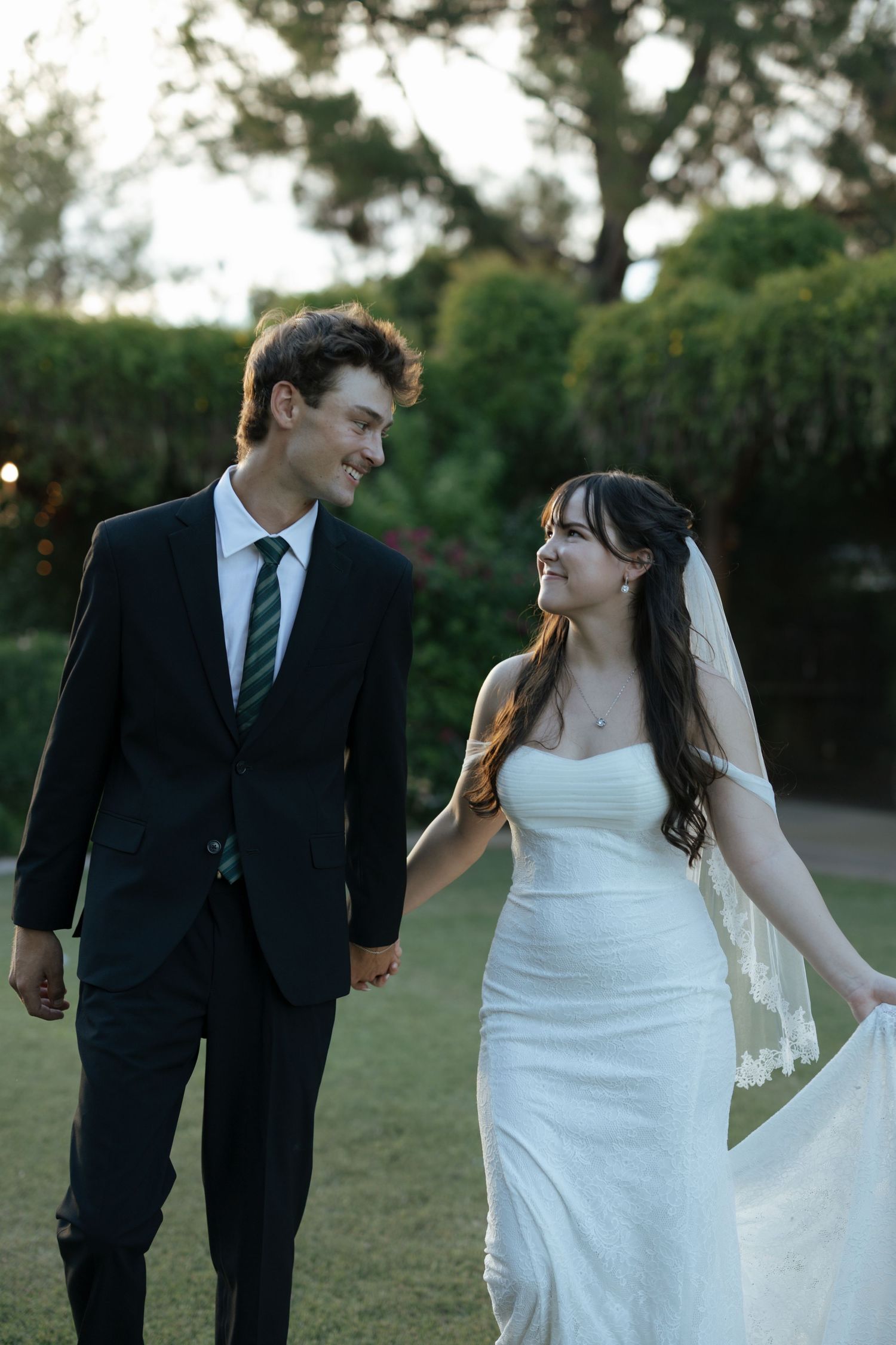 A couple in wedding attire embraces during golden hour with the bride holding a flower bouquet.