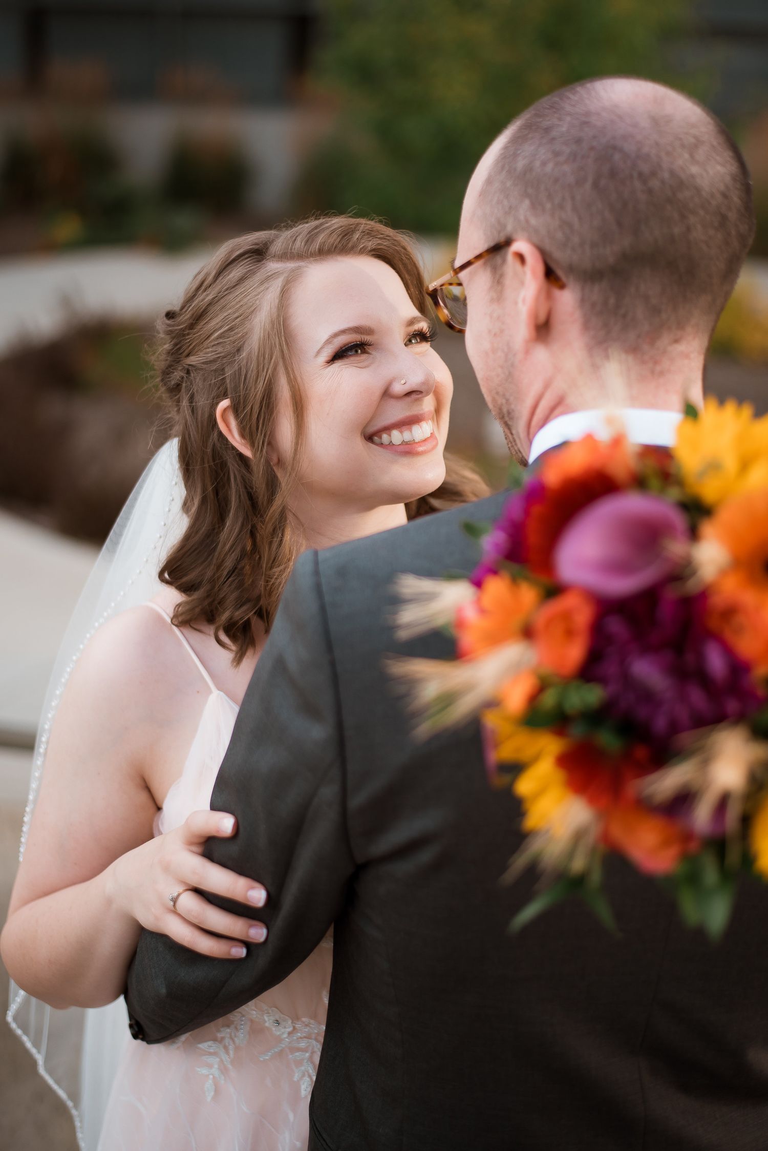 A couple shares a joyful moment at their wedding while holding a vibrant fall-colored bouquet of orange and purple flowers.