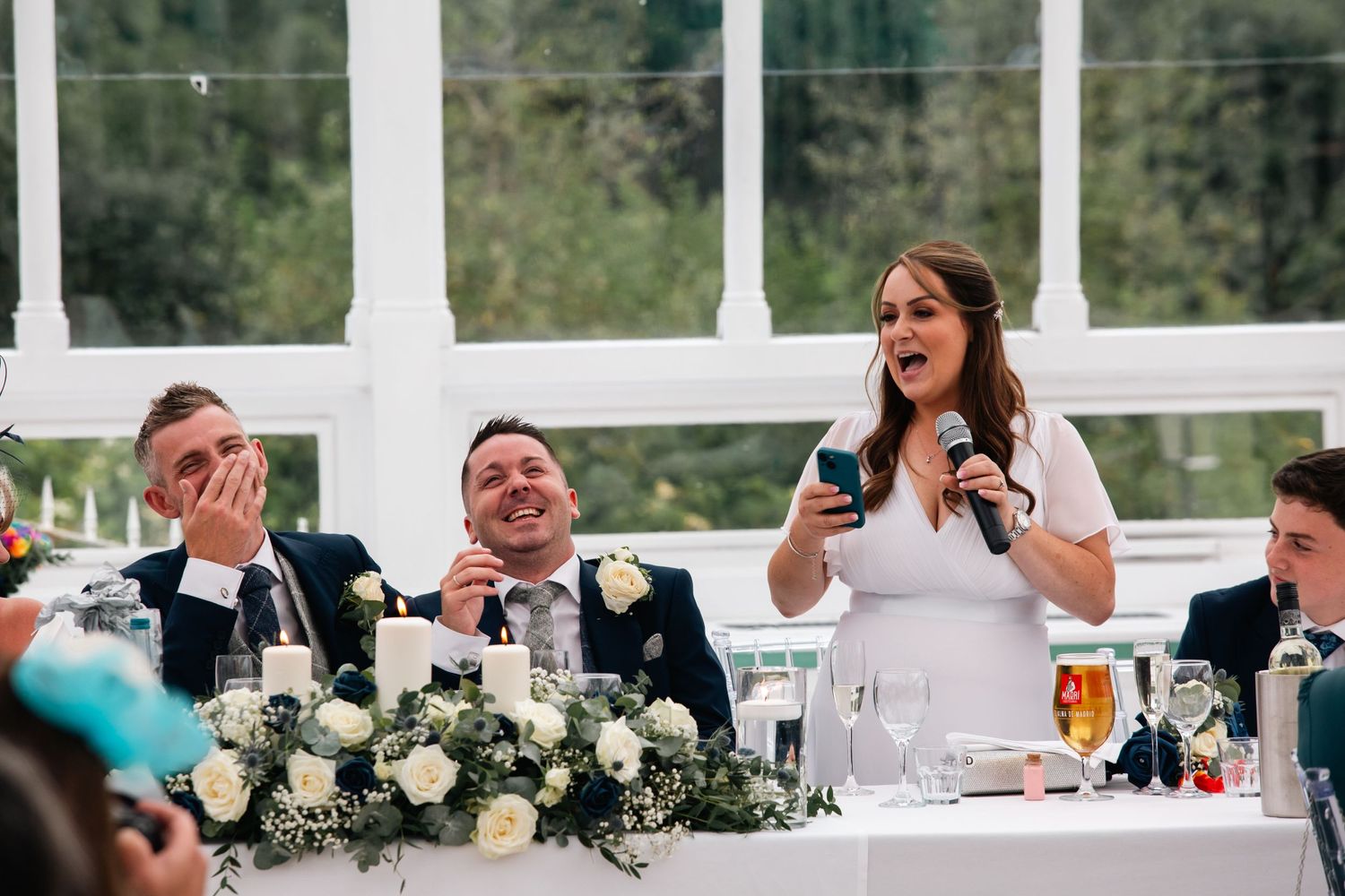 Wedding reception celebration inside elegant white conservatory with floral centerpieces.