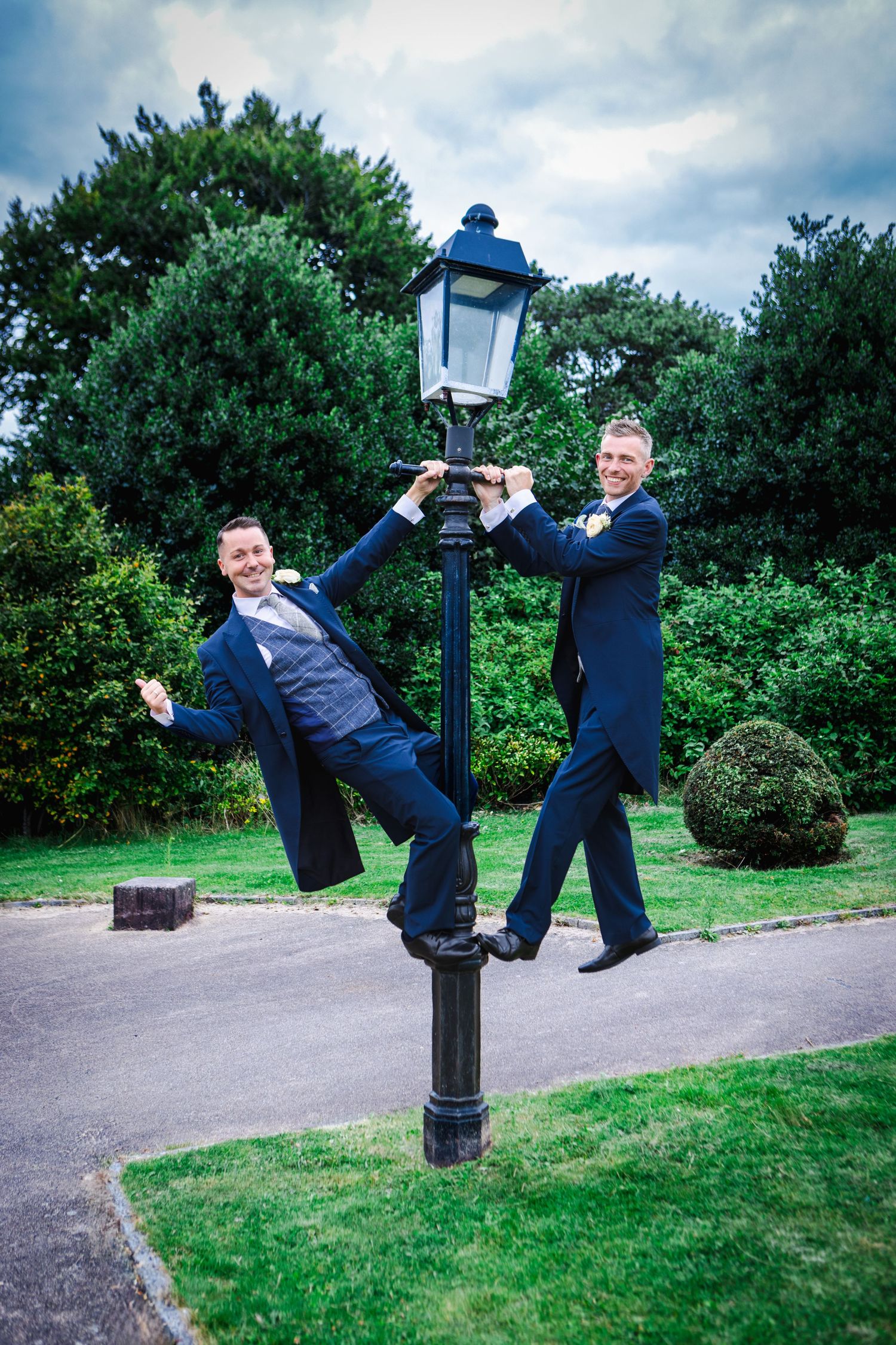 Sequence of two men in suits playfully posing near a lamppost in a park.