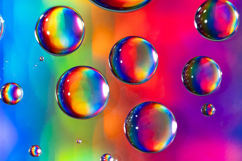 Colorful soap bubbles floating against a vibrant rainbow gradient background create a mesmerizing macro photograph.