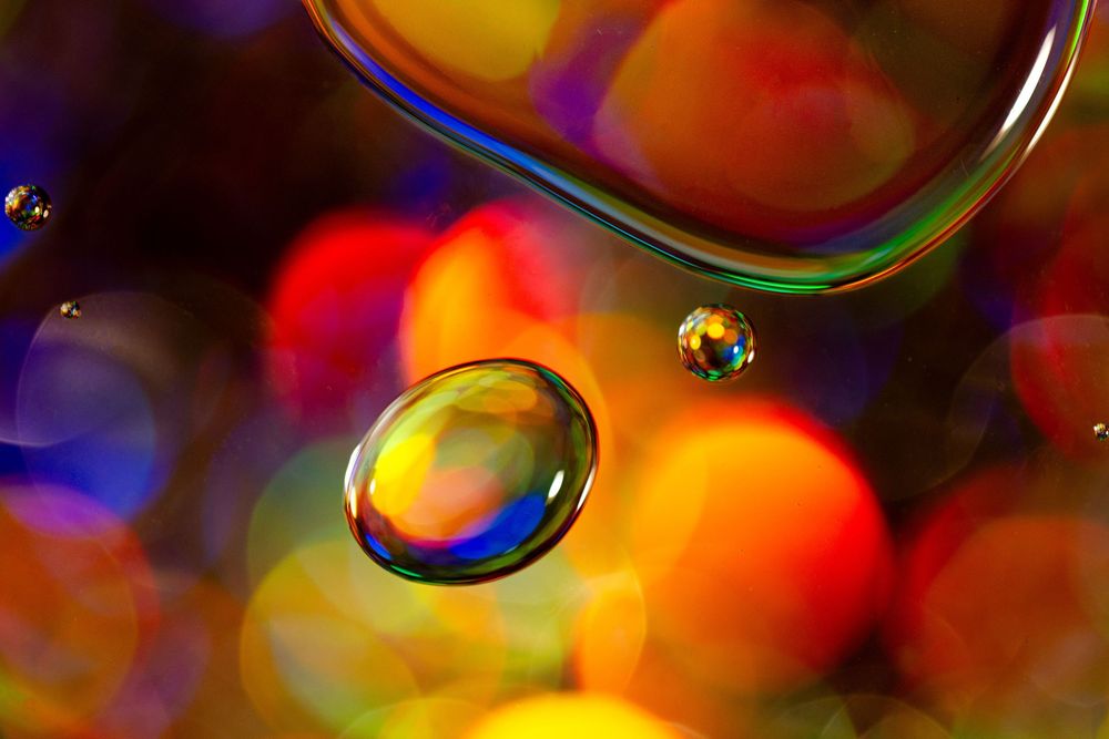 Colorful abstract macro photography of soap bubbles with vibrant orange, blue and yellow iridescent patterns.