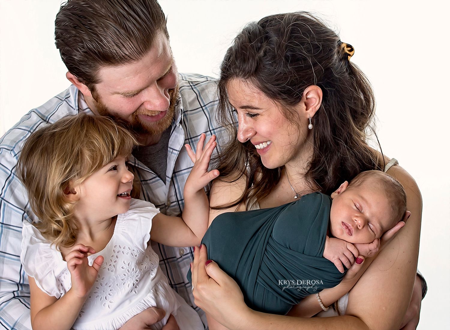 A family shares a tender moment together while holding their newborn baby in a studio portrait setting.