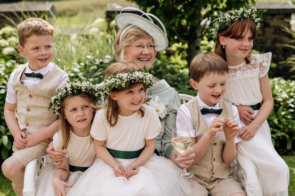 Children in formal attire and floral crowns sitting together at a wedding. All gathering around grandmother.