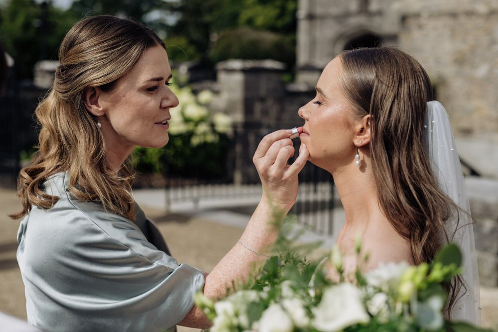 Sister applying finishing touches during cocktail hour at wedding reception outdoors.