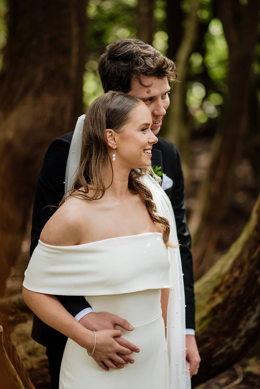 A romantic wedding portrait against mossy trees features an off-shoulder bridal gown by Dina Ozola Photography.