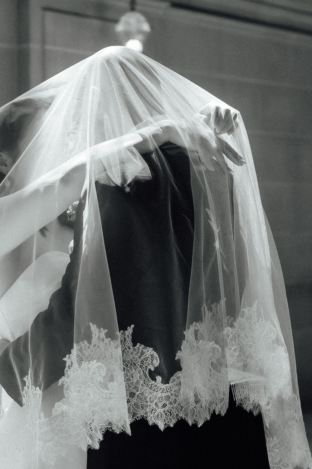 A close-up view of delicate white lace trim details on a wedding veil against a dark background.
