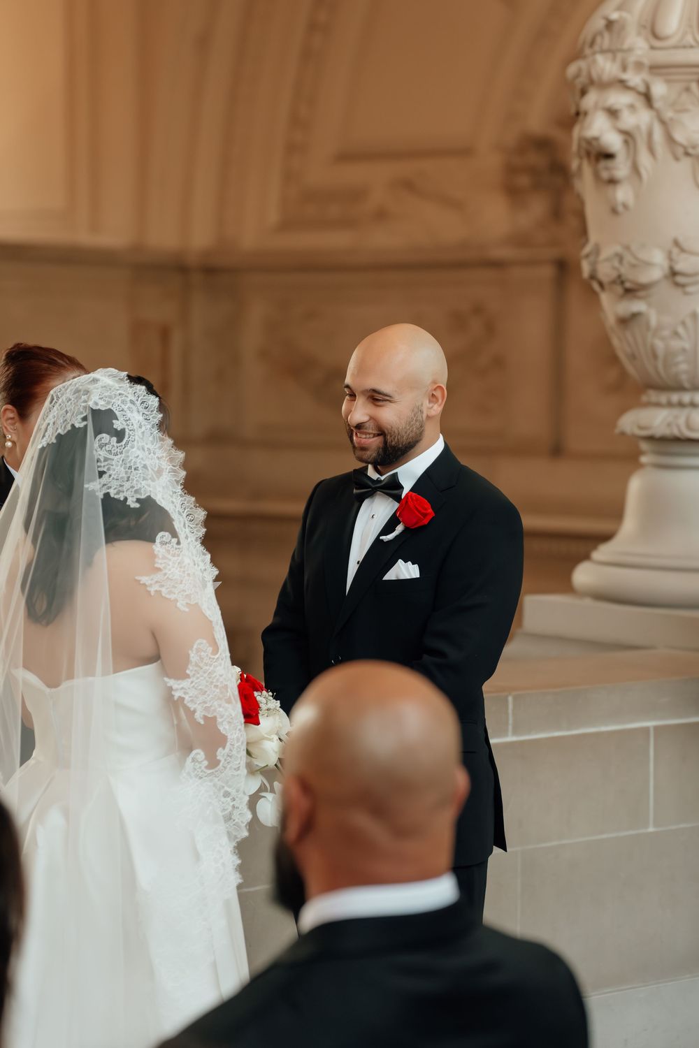 Wedding ceremony taking place in an elegant classical architecture setting with ornate columns.