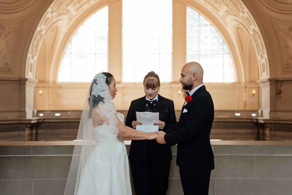 Couple exchanges vows in a grand hall with beautiful arched windows and natural light streaming in.